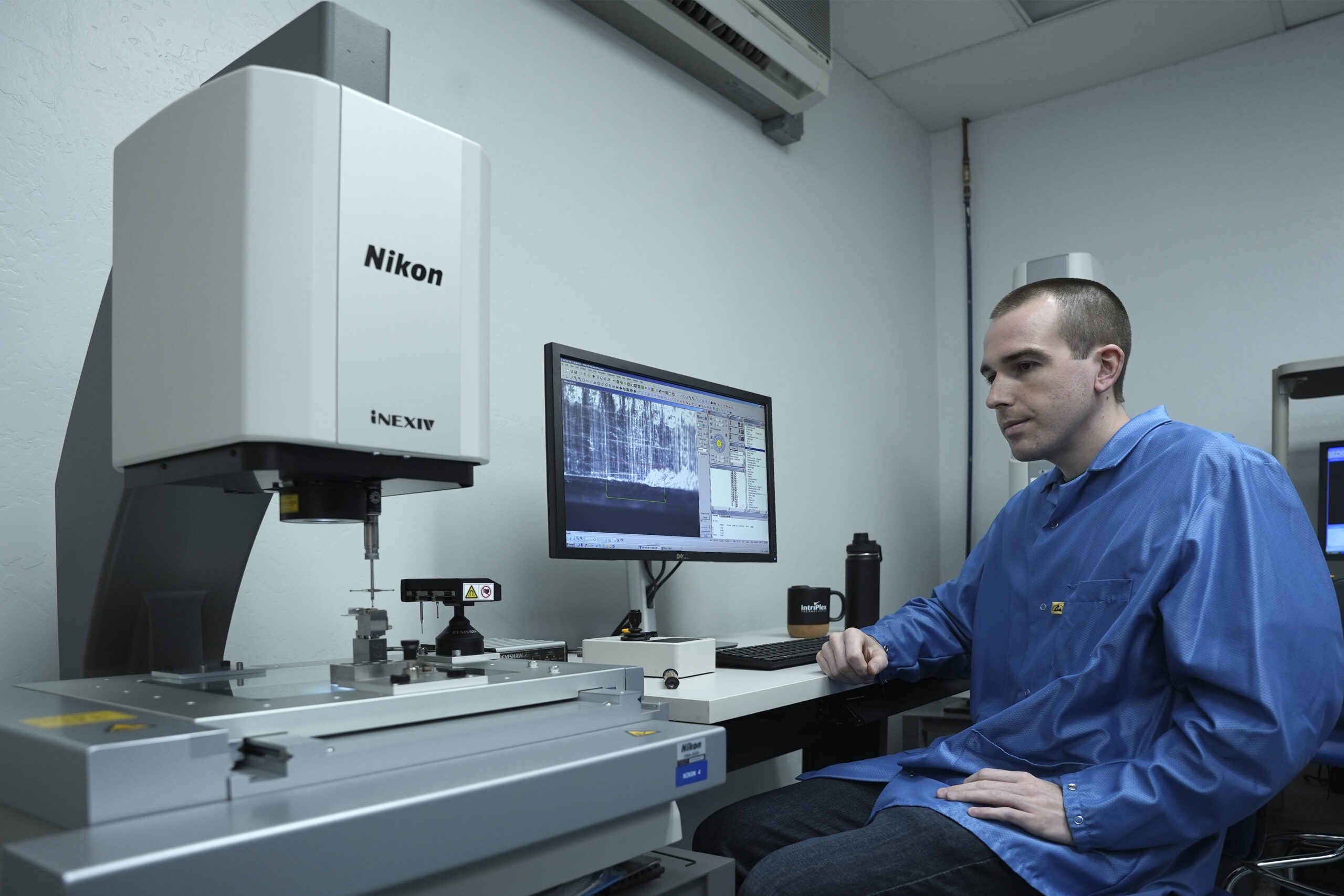 Técnico de IntriPlex en un laboratorio observando el sistema de medición por video que realiza una inspección de precisión.